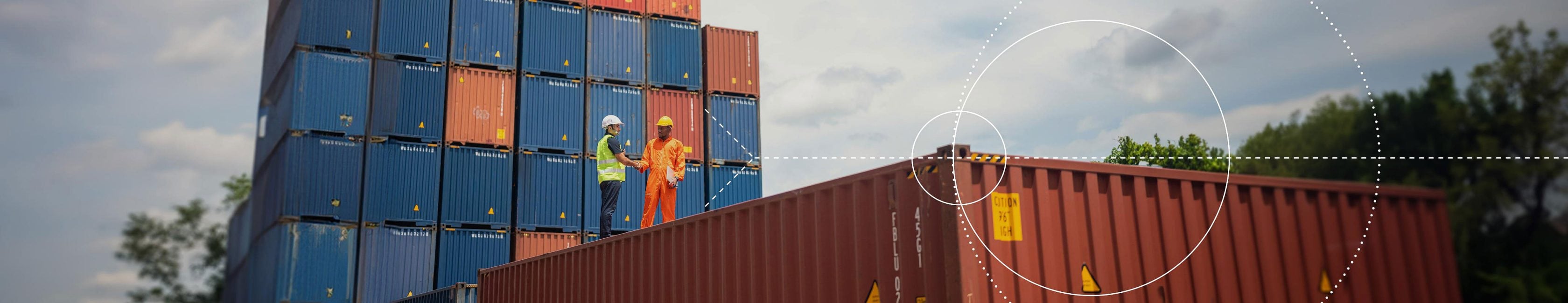Two workers standing on top of a cargo container, talking to each other, with a bench in the background Cargo containers stacked on top of each other.