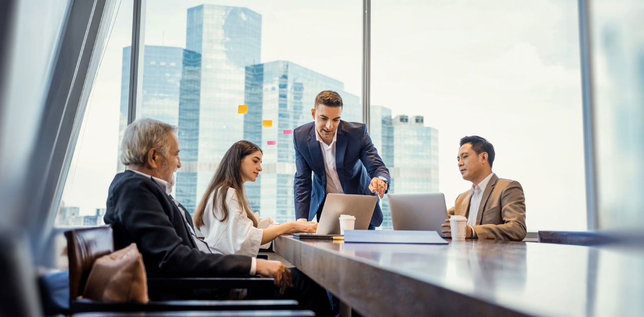 Business partners (a woman and three men) having a lively conversation at a conference table in a room with view out to skyscrapers