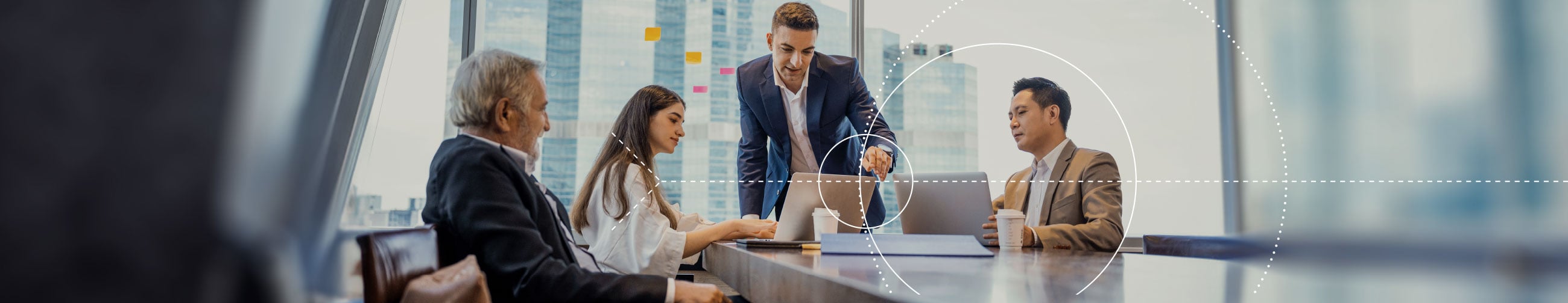 Business partners (a woman and three men) having a lively conversation at a conference table in a room with view out to skyscrapers